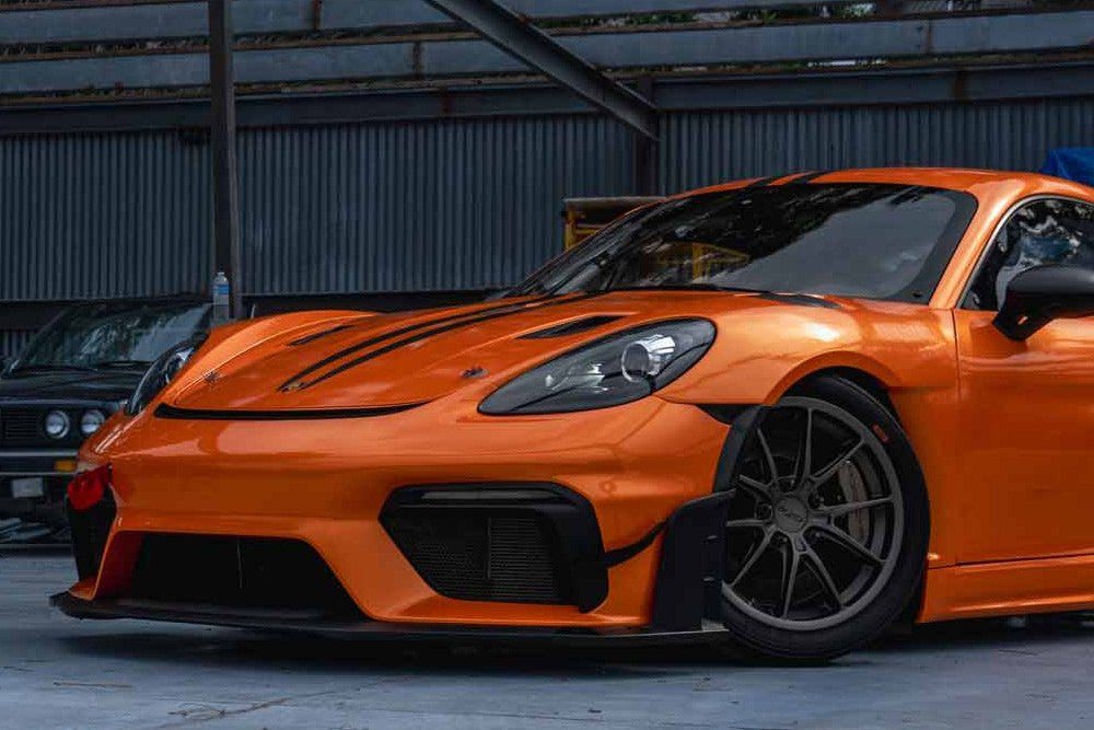 Orange Porsche Cayman with an aero kit in the shop