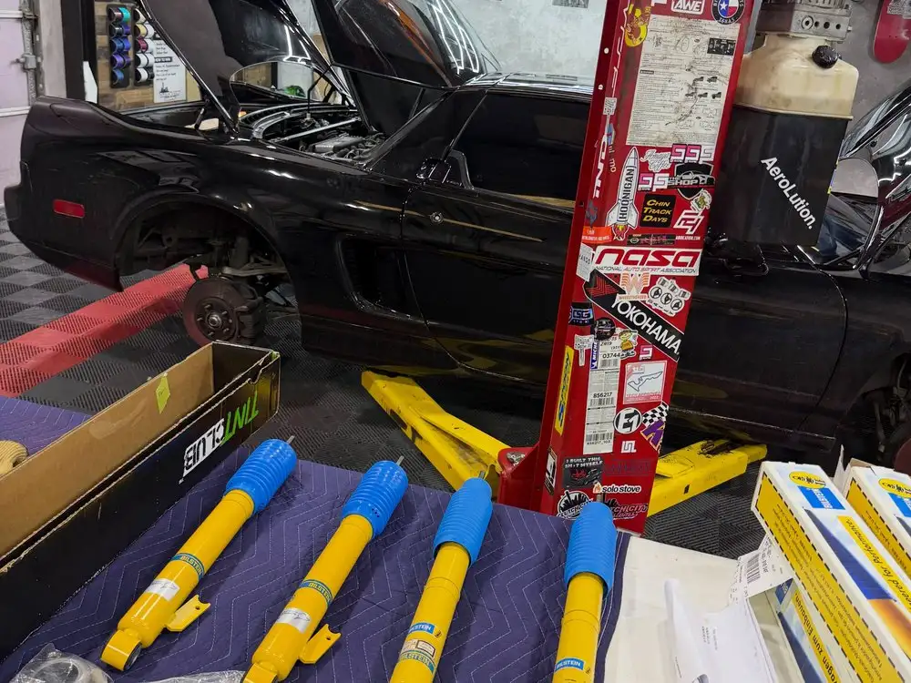 New yellow Bilstein shocks laid out beside a black car before a suspension install