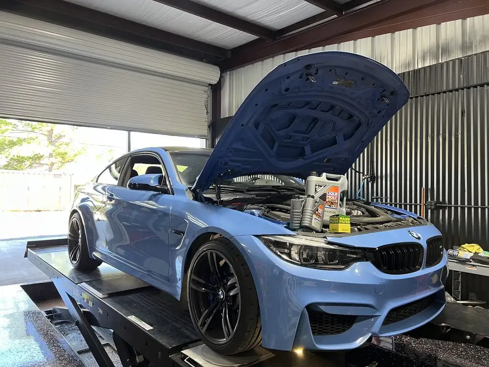 Blue BMW M4 with its hood open on a lift during an engine oil service