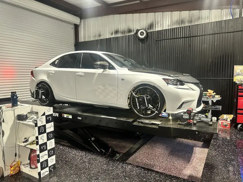 White Lexus sedan on an alignment rack with wheel targets mounted inside the shop