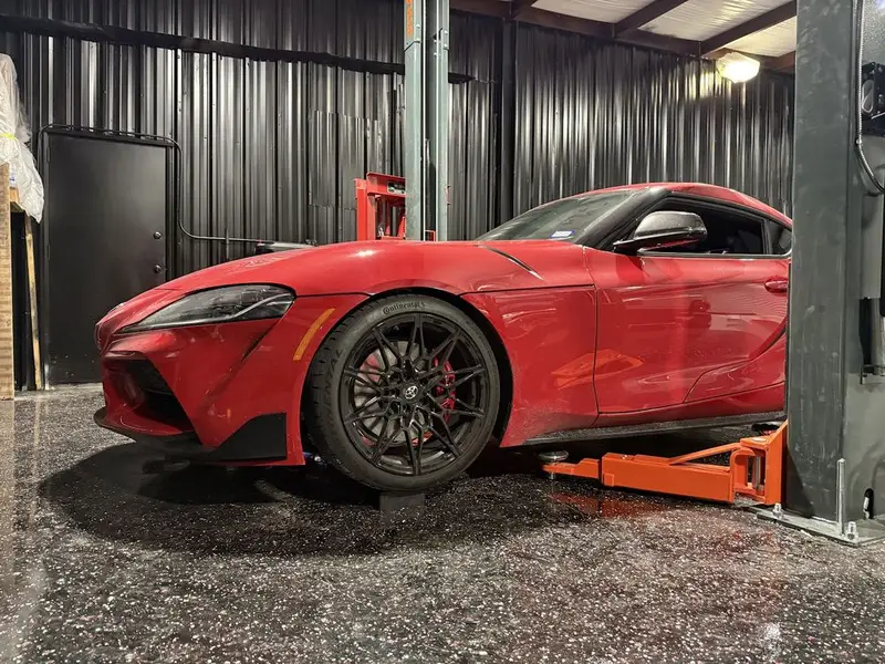 Red Toyota GR Supra raised on a lift with its wheel off the floor