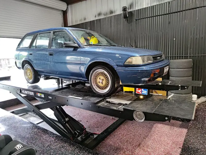 Vintage blue Toyota wagon with gold mesh wheels on a Hunter alignment rack